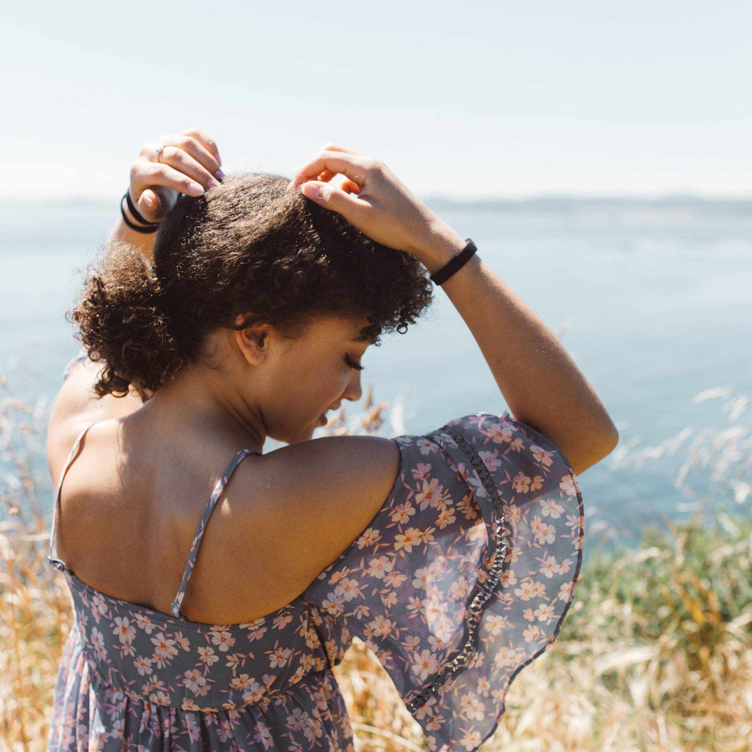 Woman with hair ties on wrists in a coastal setting.