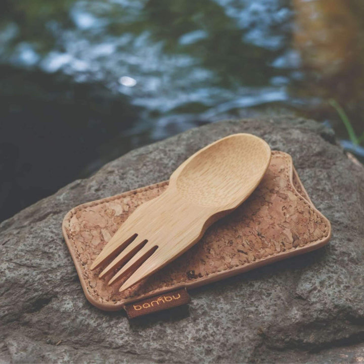 Bamboo spork atop cork case on large rock with stream in background.