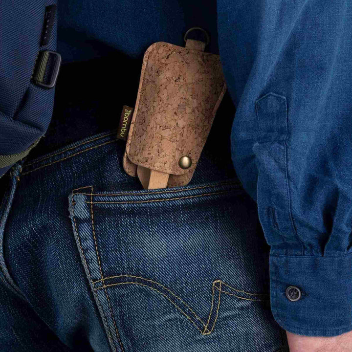 Bamboo utensil set, shown in cork sleeve tucked in back pocket of blue jeans, surrounded by corner of blue backpack and blue shirt sleeve.