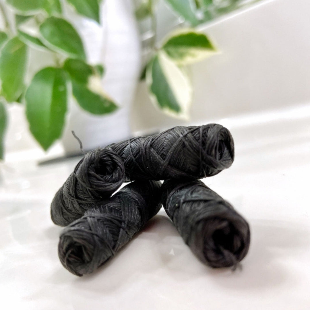 ME Mother Earth Charcoal Dental Floss 4-pack Refills Out of Box, Shown Stacked on White Countertop with Houseplant in Background.