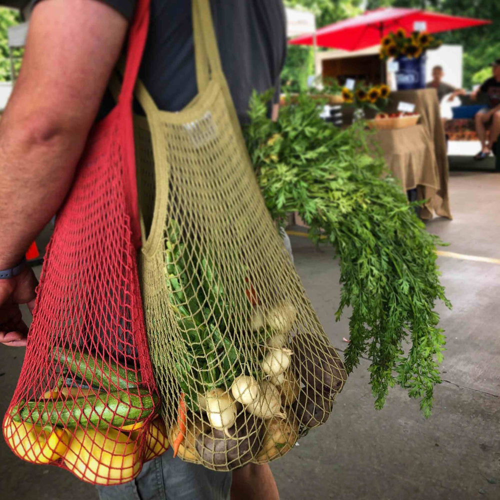 EcoBags String Shopping Bags in Chili and Celery Colors, filled with fresh produce and hanging from man's shoulder at farmer's market.