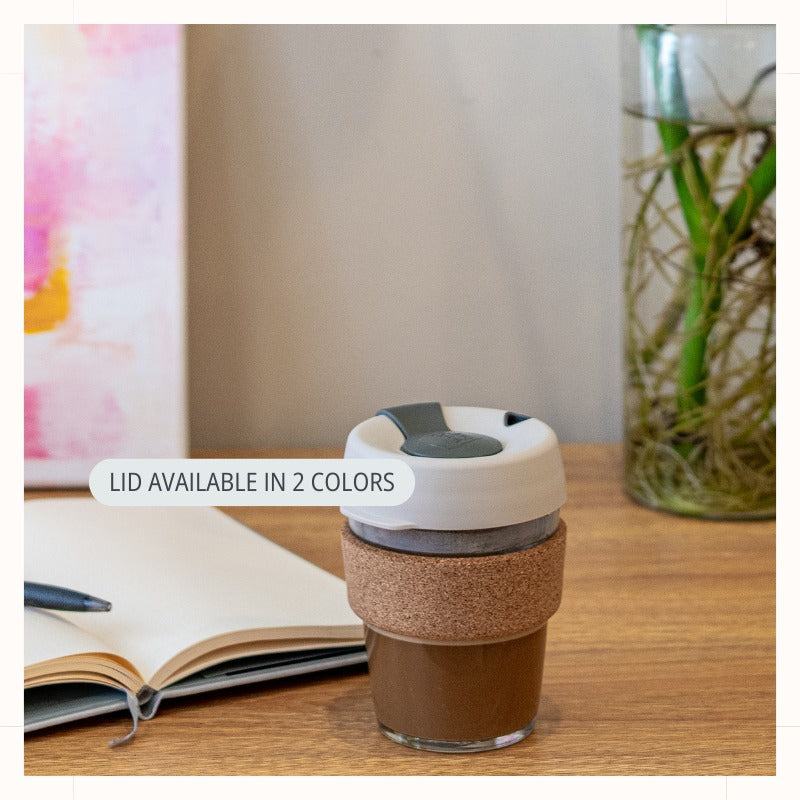 Glass Coffee Cup with Lid and Cork Band in Filter/Beige color filled with coffee on desk. Note indicated lid is available in 2 colors.