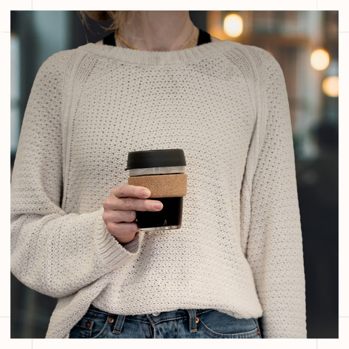 Glass Coffee Cup with Lid and Cork Band in Press/Charcoal color held in held by woman.