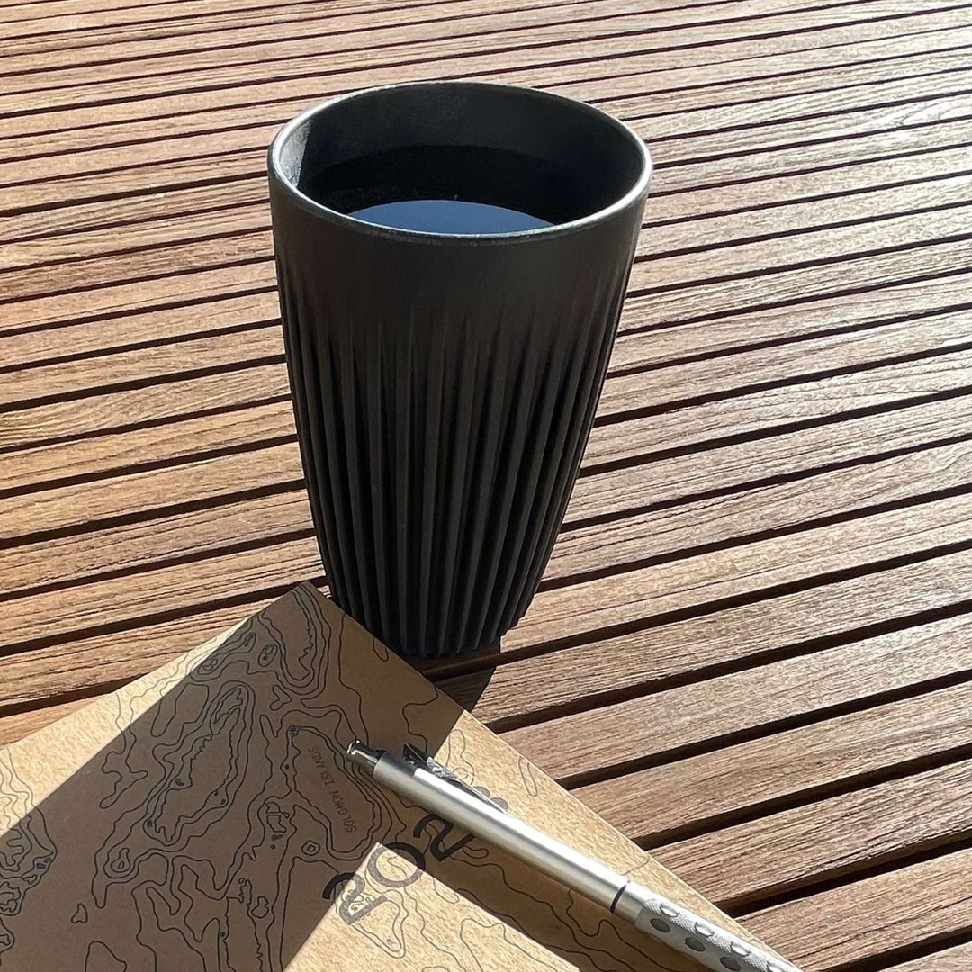 HuskeeCup and lid in charcoal color, shown on wood table with zero waste planner and metal mechanical pencil (not included).