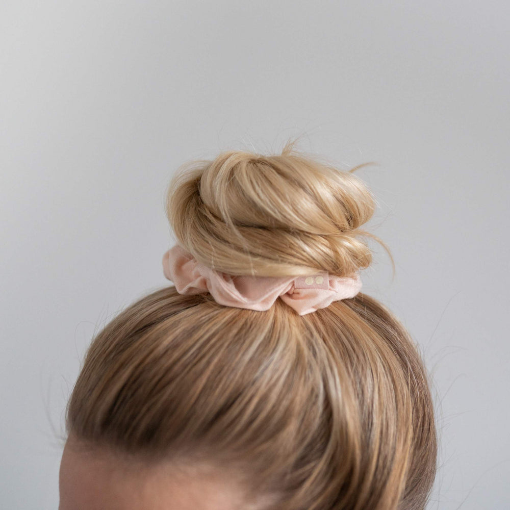 Top knot in woman's hair, secured by hair scrunchie.
