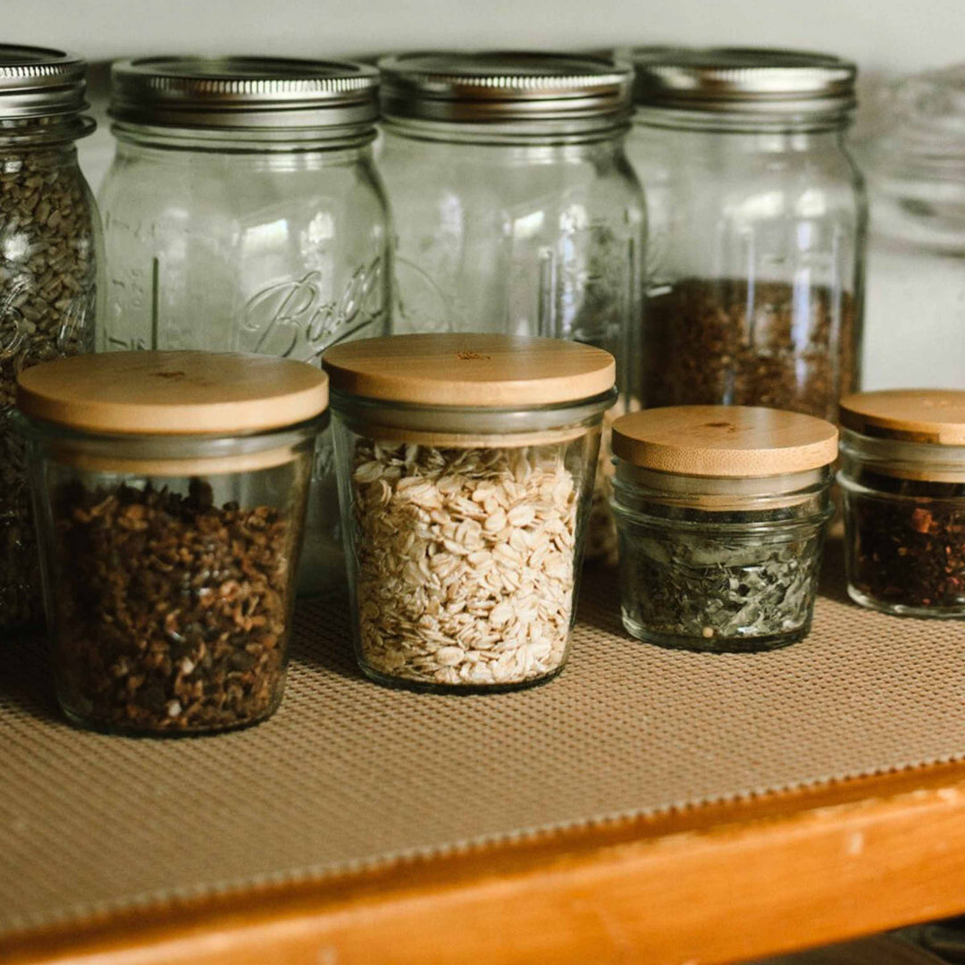 Bamboo Mason jar lid (wide size on left) shown on pantry shelf with other glass jars behind.
