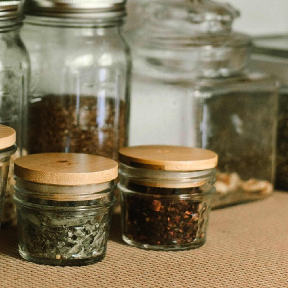 Bamboo Mason jar lids shown on small glass jars with for food storage. Other glass canisters in background. 