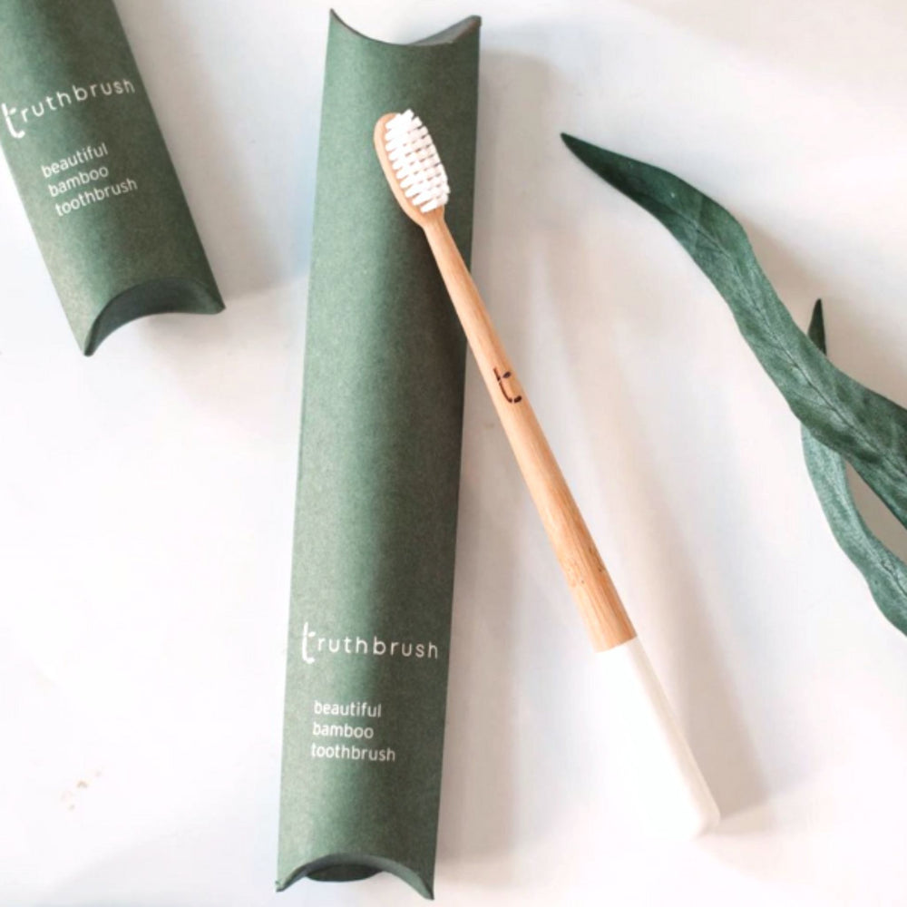 Bamboo Toothbrush for Adults - Medium Bristlesin Cloud White color with medium bristles, shown with plastic-free packaging in middle and left, and plant leaves on right.