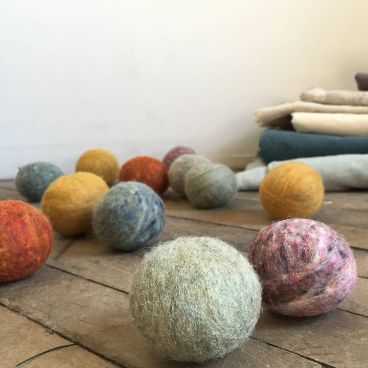Bog Berry Wool Dryer Balls in Earthy Heathers, Shown on Wood Slats with White Wall and Folded Fabric in Background.