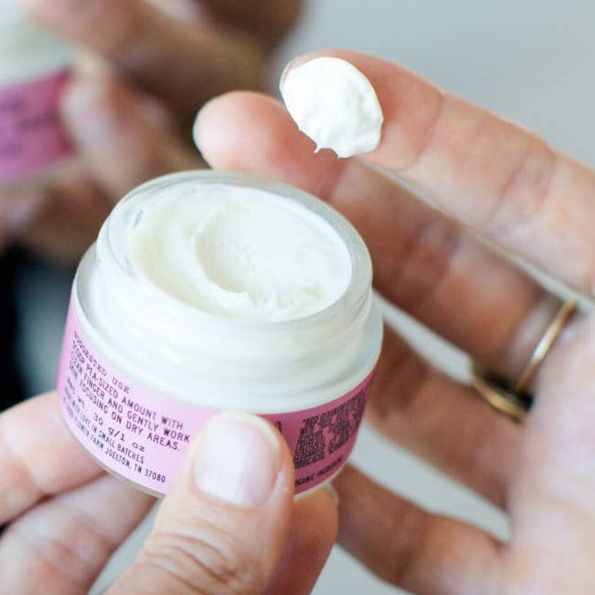 Good Flower Farm Organic Rose Geranium Face Cream In Glass Jar, In Use With Dab Of Cream On Finger.