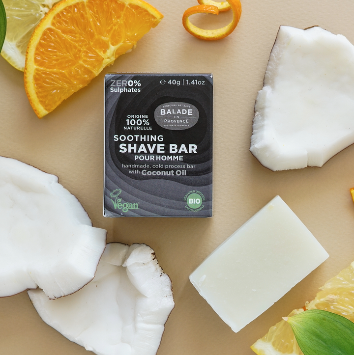 Handmade, cold process, vegan shave bar for men in paper packaging, surrounded by pieces of coconut and citrus slices.
