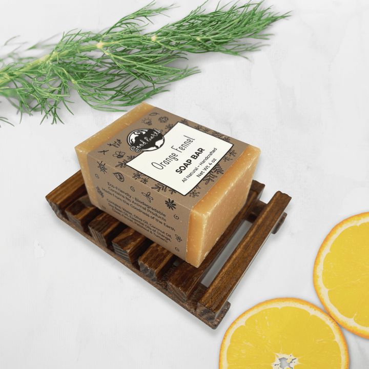 Good Earth Orange Fennel Soap Bar In Simple Sleeve Packaging Atop Wood Soap Dish (Sold Separately). Shown With Fennel Sprig And Two Orange Slices.